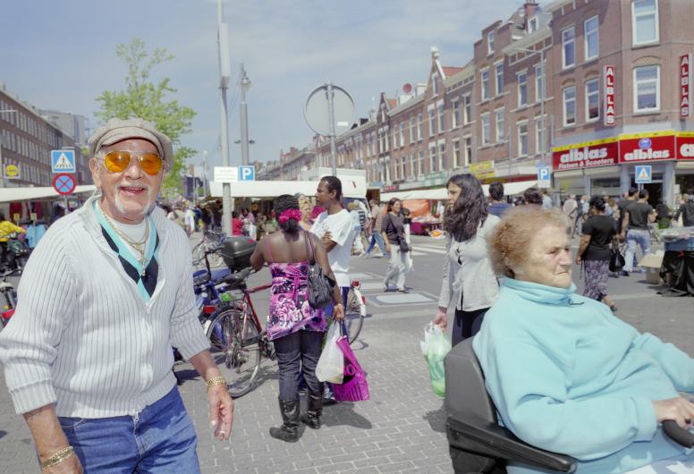 Lopende man en vrouw op scootmobiel in de voorgrond, achtergrond Afrikaandermarkt