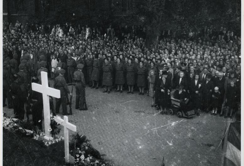 Zwart wit foto van een groep mensen verzameld bij een herdenkingskruis op de Oostzeedijk