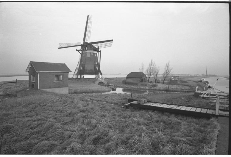 Zwart-wit foto van een molen op een hoger gelegen stuk, rechts en links ligt water.