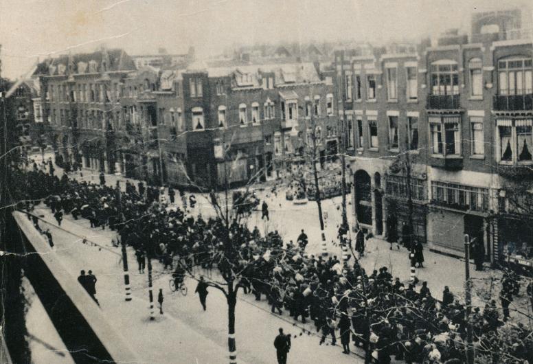een groep mannen wordt door de straat begeleid door soldaten voor afvoering naar werkkampen