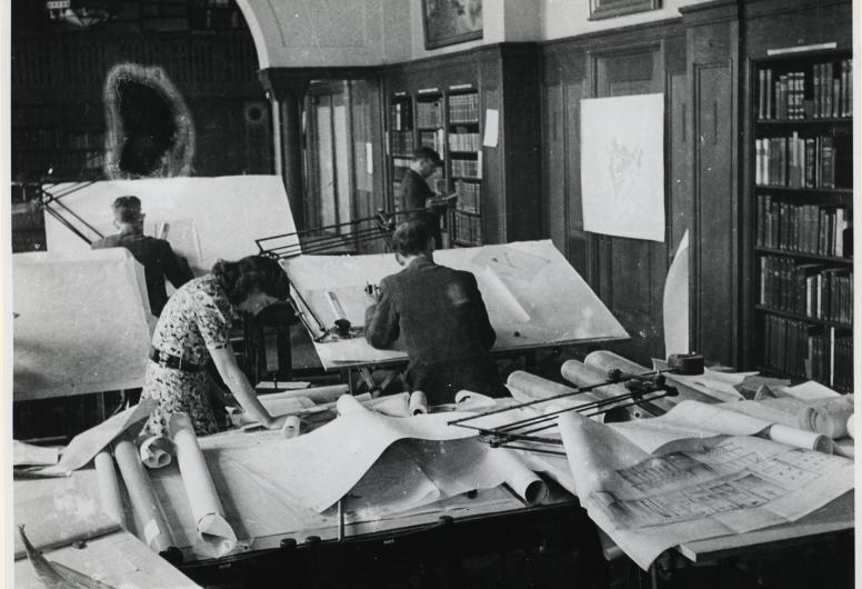 Medewerkers achter tekentafels in kantoren van het ASRO in de Gemeentebibliotheek.
