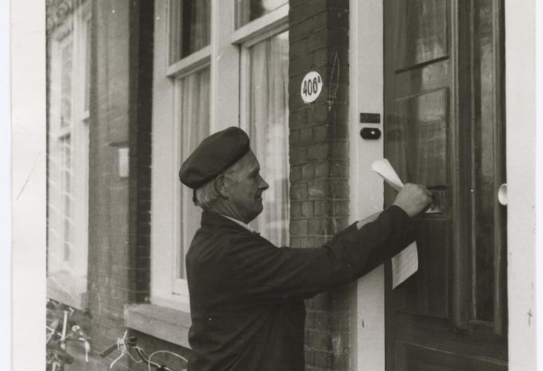 Op de afbeelding is een medewerker van de ROTEB een flyer in een brievenbus aan het stoppen. Deze verspreidt de ROTEB huis-aan-huis om iedereen van de juiste informatie te voorzien.