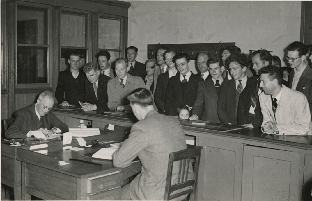 Groep mannen achter een balie kijkt toe bij een geboorteaangifte bij de burgelijke stand in Rotterdam