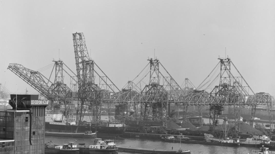 Binnenvaartschepen liggen in de Waalhaven bij de overslag van kolen. Op de voorgrond links het gebouw van de Rotterdamse Kolen Centrale (Rokocent). Op de achtergrond staan kranen op Pier 5.